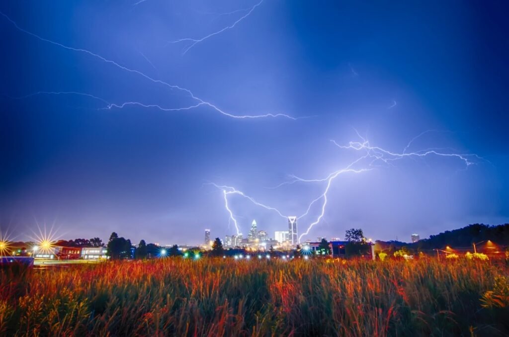 Lightning bolts striking above a city at night with a field in the foreground.